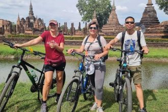 Cyclistes devant les chedis et l'étang du parc historique de Sukhothai
